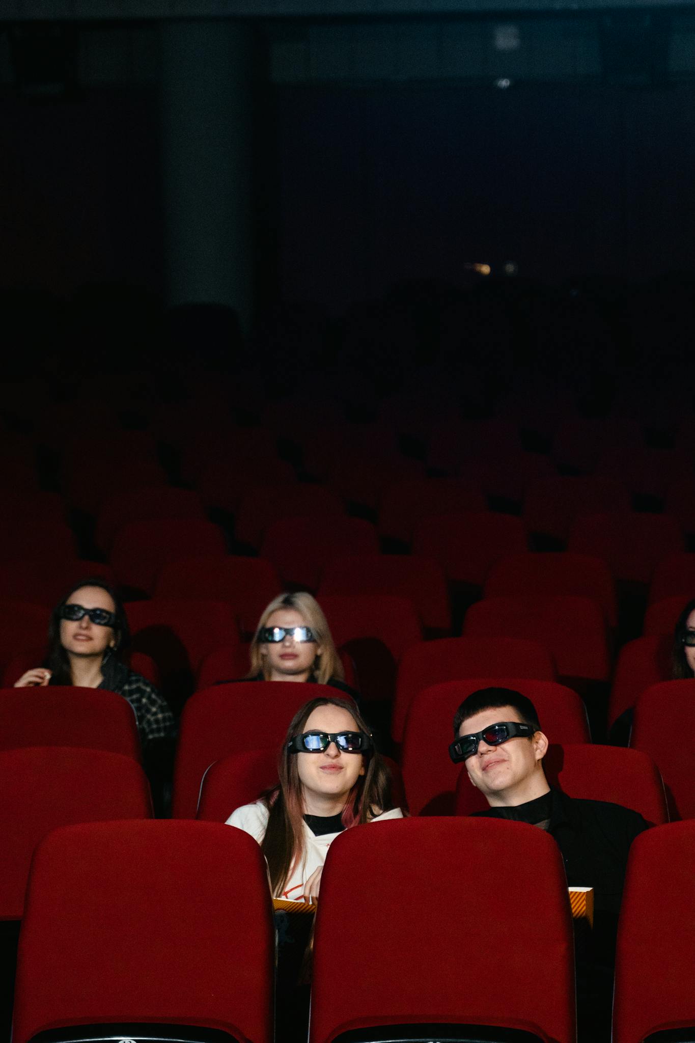 Audience seated in a cinema wearing 3D glasses, enjoying a movie indoors.