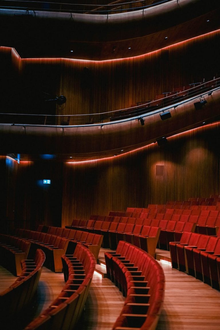 A beautifully lit theater with curved rows of red seats and wood paneling.