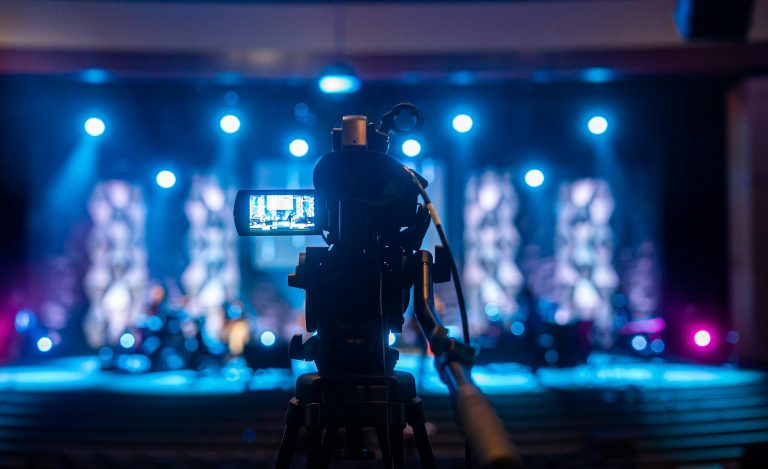 Video camera capturing a vibrant concert scene under bright stage lights.