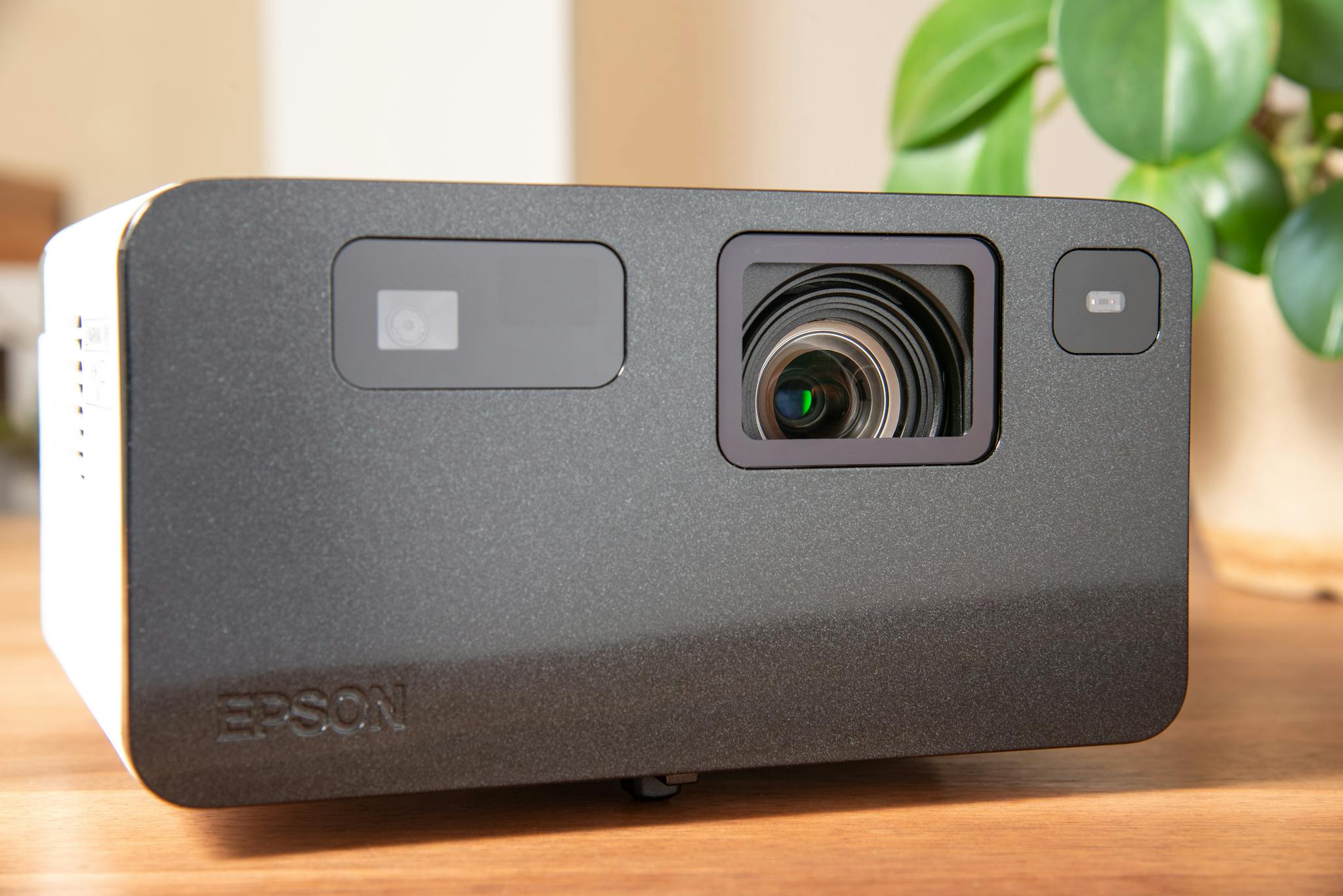High-quality product shot of a modern Epson projector on a wooden table with indoor plants.
