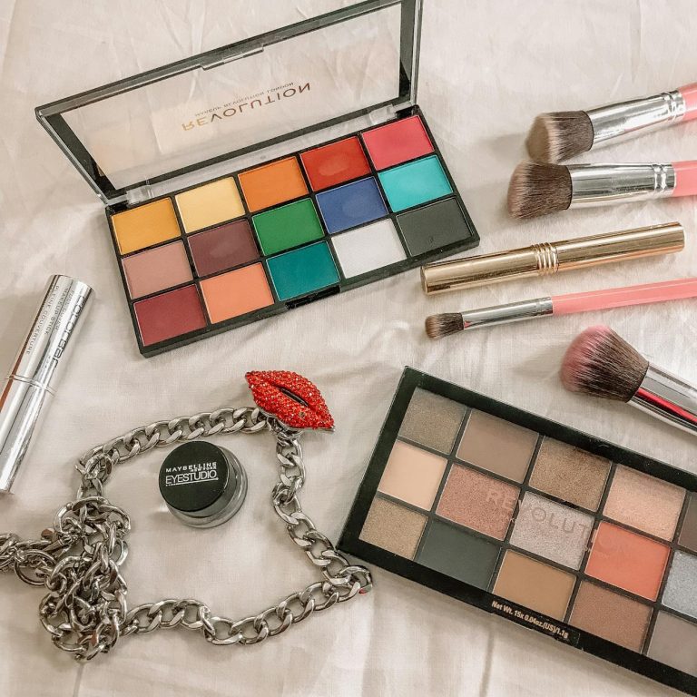 A creative flat lay of makeup palettes, brushes, and accessories on a bright surface.